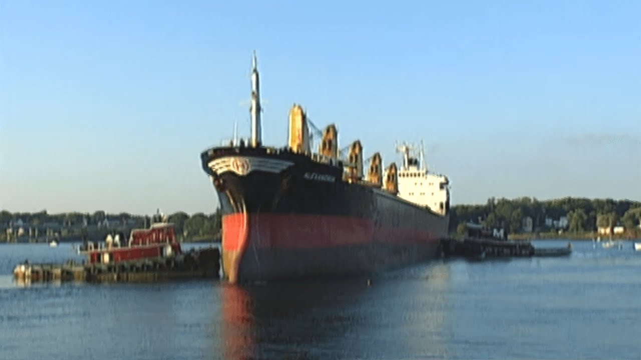 big tug boats push a giant ship into harbor where coal is