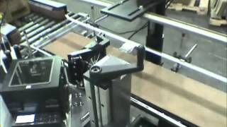 A Label Printer Applicator with Integrated Conveyor applies a label around the corner of a box