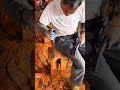 Chiseling large wooden piece with mallet while sitting on it with many orange wood shavings on floor