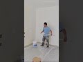 applying white paint on the wall using a long extension roller brush to cover the upper corner areas
