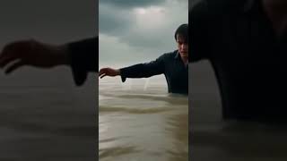 A dramatic low-angle tracking shot at water level. A man is chest-deep in a