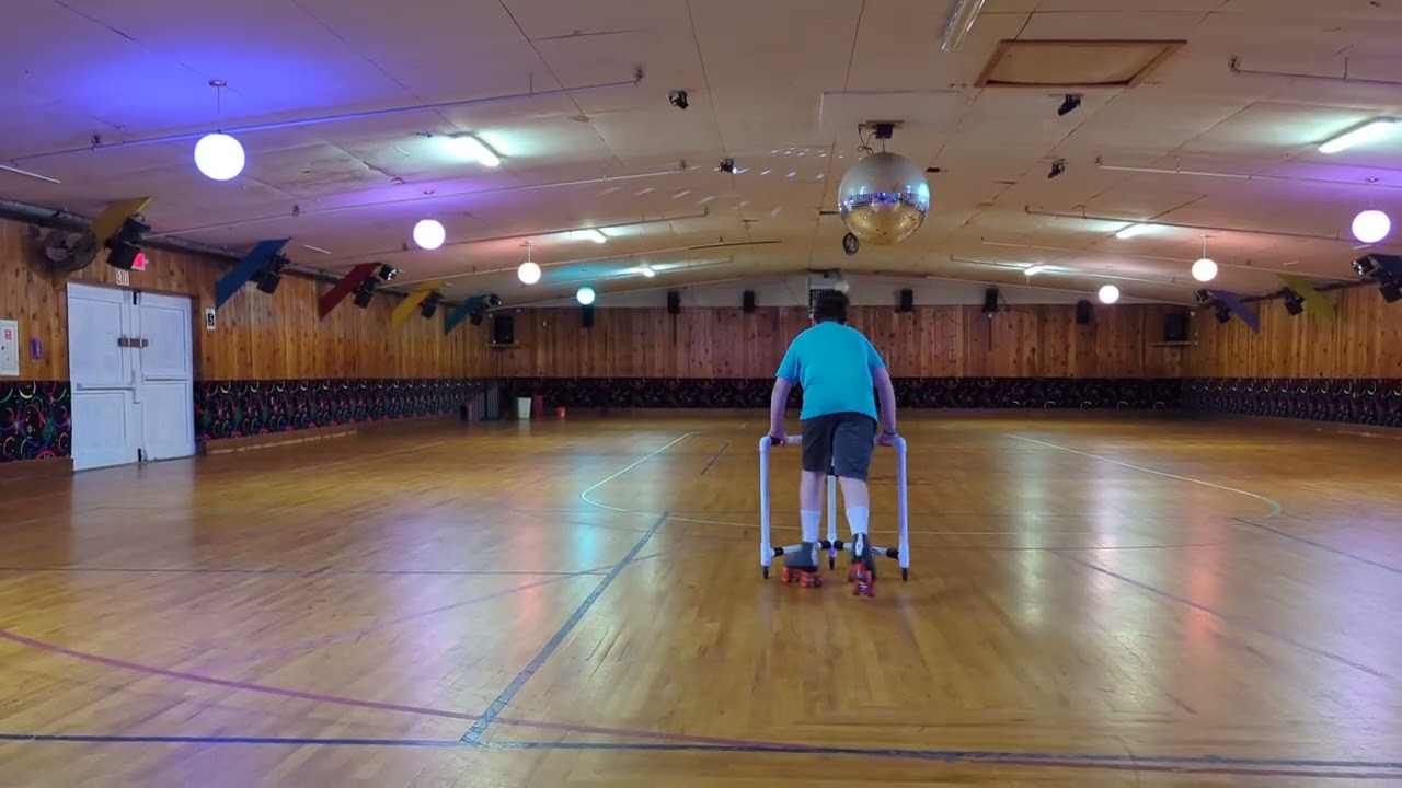 Boy roller skates for first time in roller rink and uses trainer then falls back and lands on rear