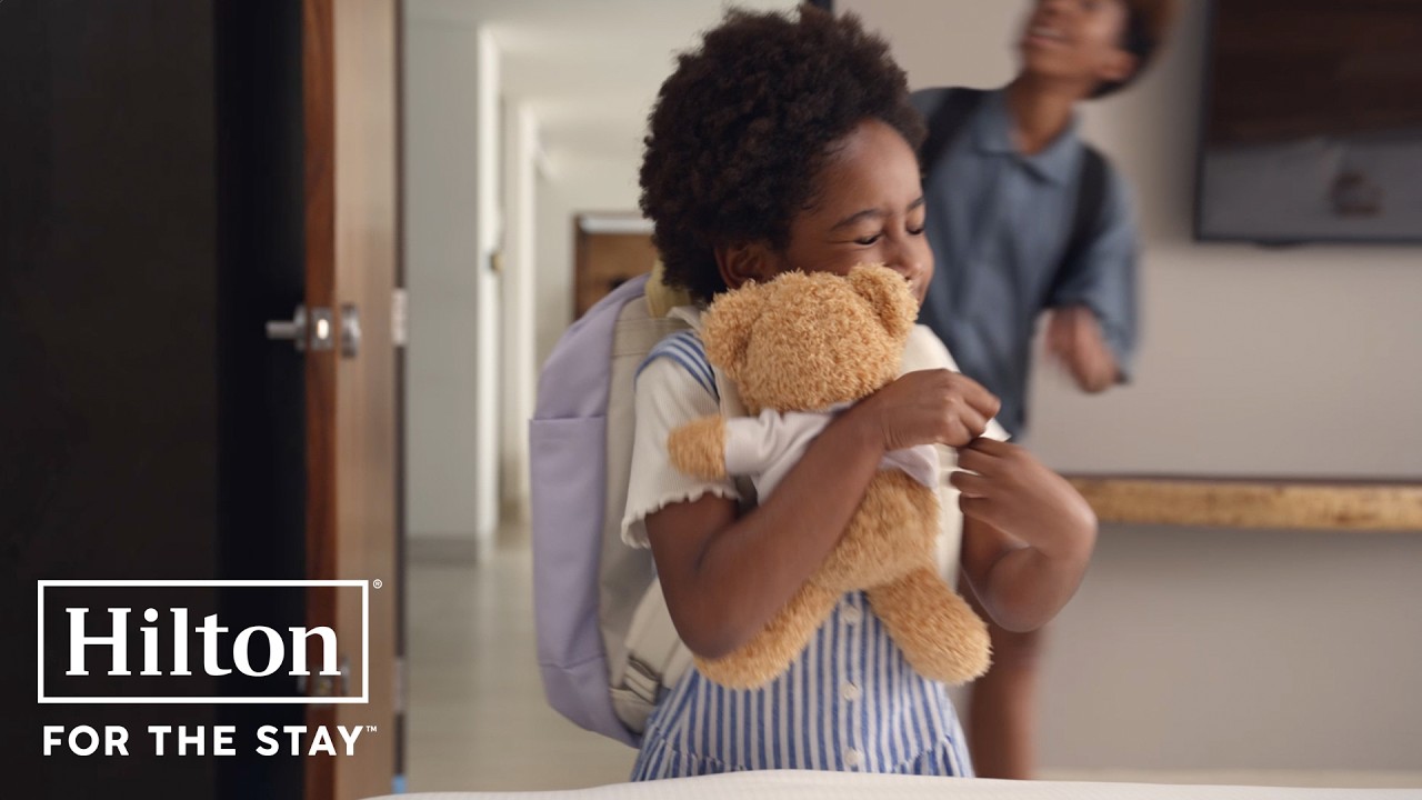 The ad opens with a family of five crammed into a hotel bed, looking uncomfortable. The scene then shifts to the same…