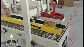 Automatic box tape sealer folding and sealing boxes on a roller conveyor