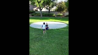 Boy sits on bucket being used as soccer goal then bother kicks ball and hits him on face (Drone cam)