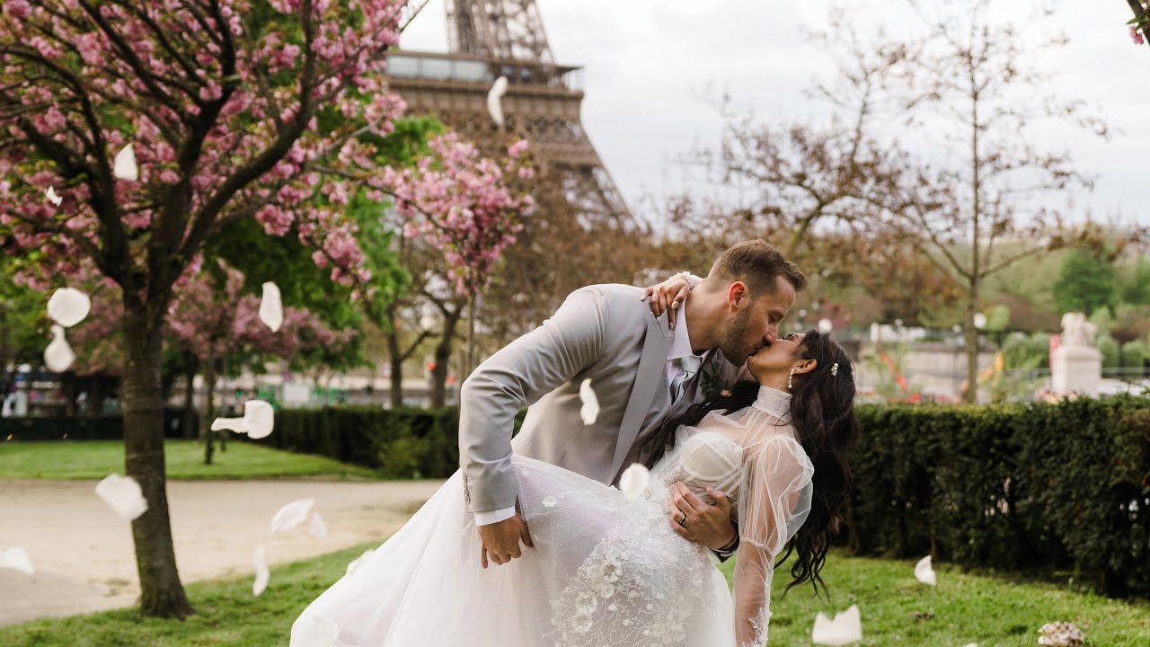 Bride and groom kiss in a Paris garden with the Eiffel Tower behind them as petals fall