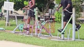 Minister Alexander exercises on an outdoor air walker as workers install the Police-Army Post on Sun