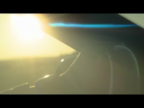 Hand with wrist watch turning steering wheel in sunset, anamorphic flares