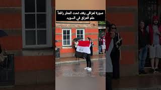 عراقي في السويد يقف تحت المطر رافعا علم بلاده