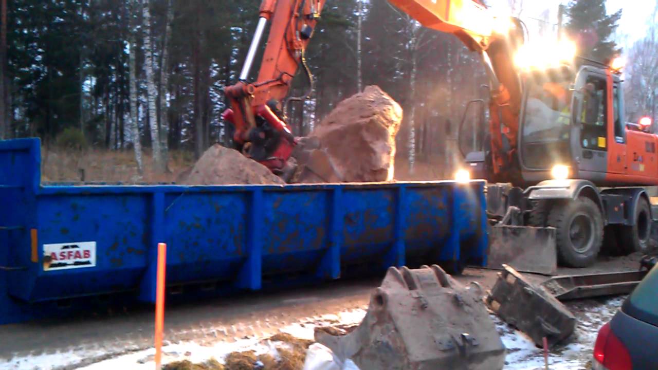 Hitachi EW160 lastar en sten på lastväxlarflak.
