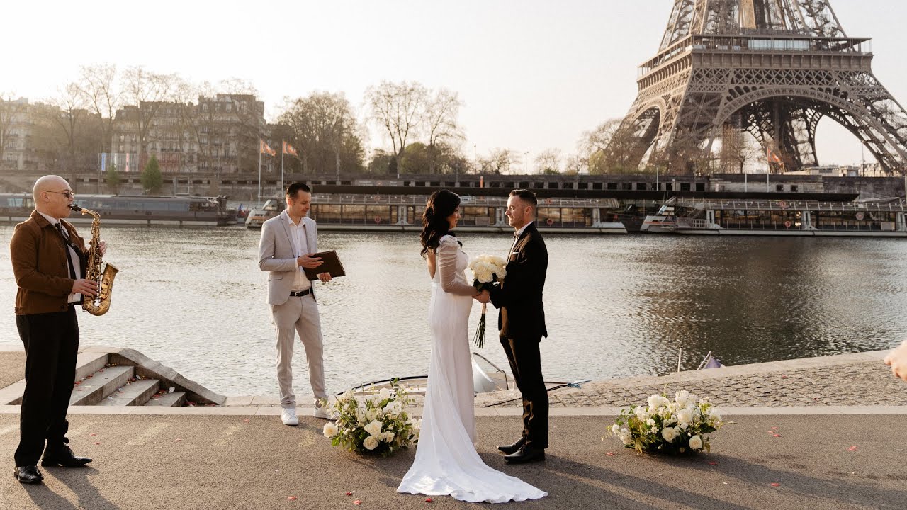 Bride and groom exchange vows by the Seine near the Eiffel Tower as an officiant and saxophonist stand in warm light