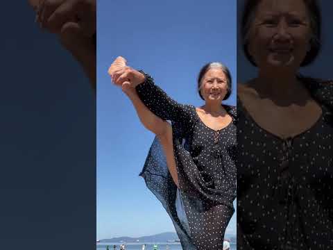 Granny in her 70s balancing on one leg on the beach
