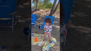 Girl standing on beach towel gets hit on back of head by lounge chair from gust of wind