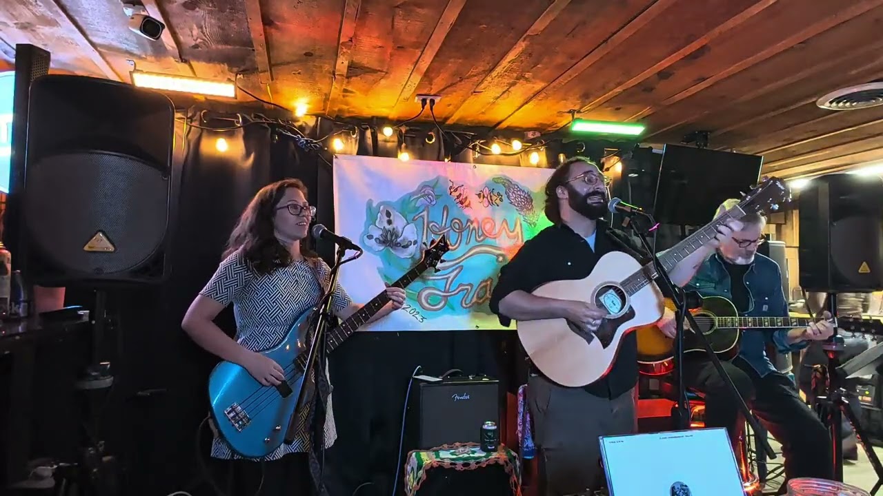 Honey Trail on stage under string lights, with their painted Honey Trail banner behind them.