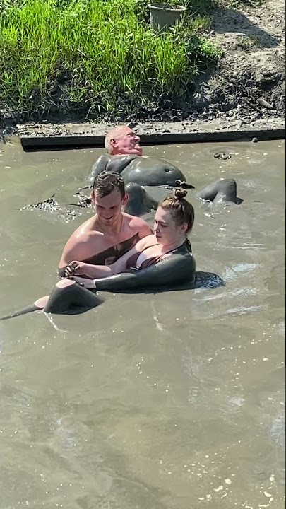 Man helps a disabled woman into a mud bath.