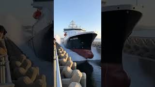 Rebound waves stack and spread as the ship enters calm water between massive concrete walls.