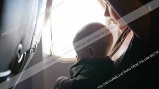Baby Sitting On Mothers Lap On An Airplane During Flight. He Looks Around And Touching The Belt