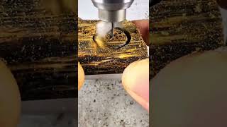 Drilling a precise circular hole into a piece of dark wood using a high speed electric drill press