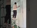 standing on a ladder and using a putty knife to patch small holes or cracks on the wall with white