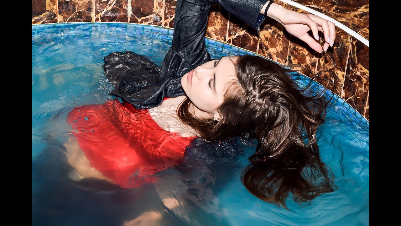 cute student girl playfully posing in wet clothes in interior with swimming pool for wetlook video