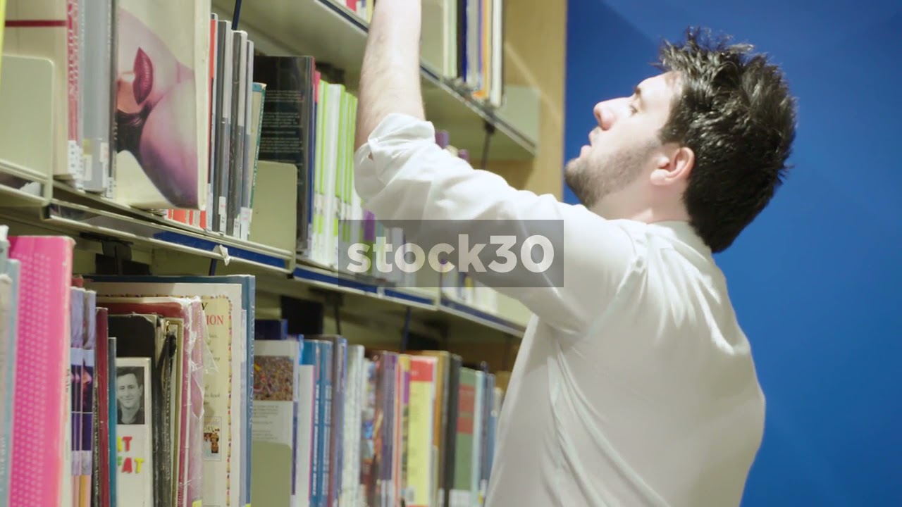 Man In Library Selecting And Looking Through Books