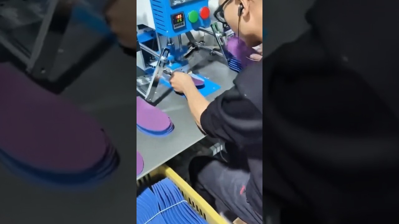 stamping small purple fabric insoles using a blue industrial heat press machine inside the factory