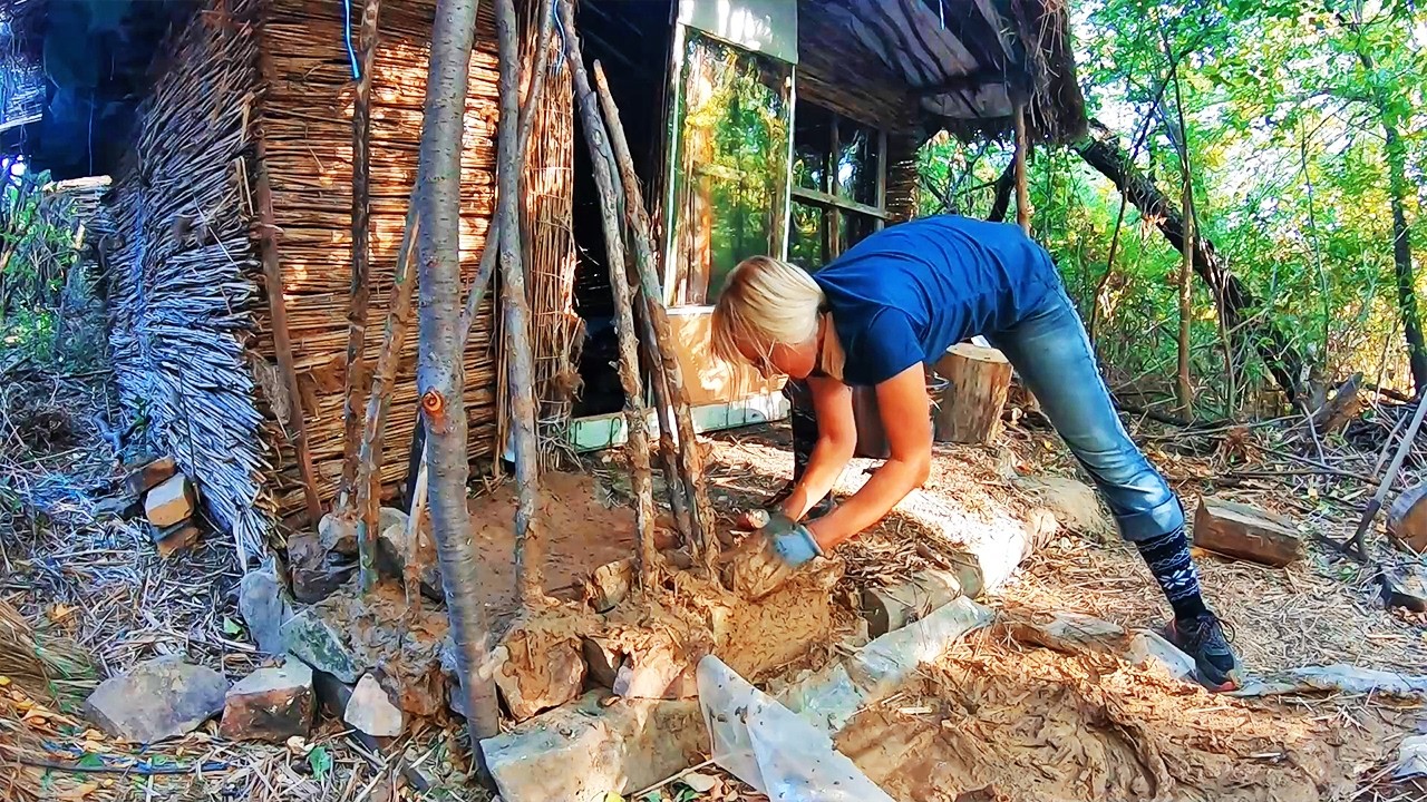 Woman builds a reed hut alone. A clay fireplace and wall insulation ...