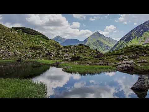 Ein 29-sekündiges Zeitraffer-Video einer alpinen Berglandschaft in Österreich. Schnelle, dynamische Wolkenformationen ziehen über schroffe Berggipfel und schattige Kare hinweg, während sich Licht und Schatten rasant auf den grünen Berghängen und den glasklaren Seeoberflächen verändern.