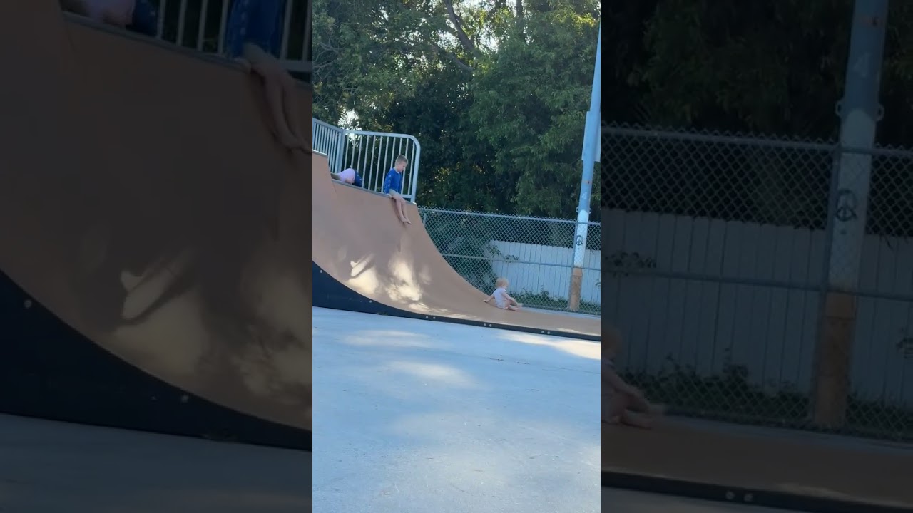 Boy slides down from top of halfpipe then crashes into baby seated at bottom of ramp