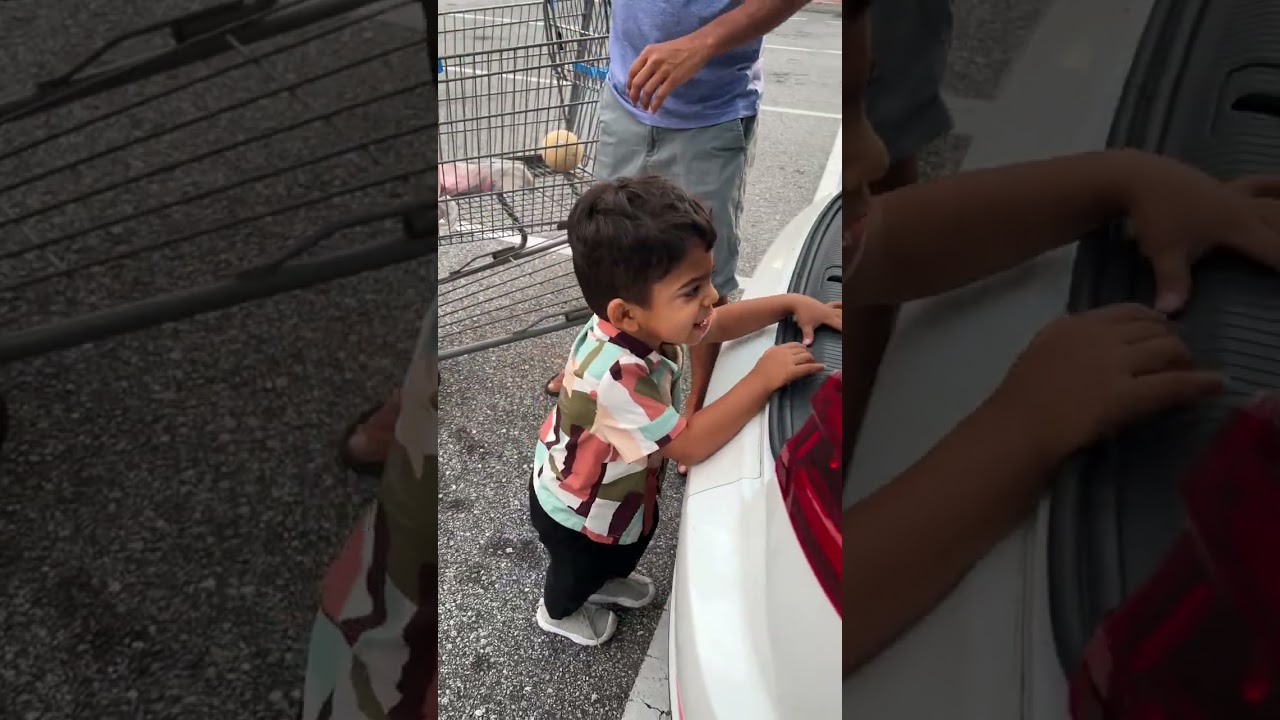 Boy opens car door and bumps head while Mom and Dad are packing groceries from supermarket