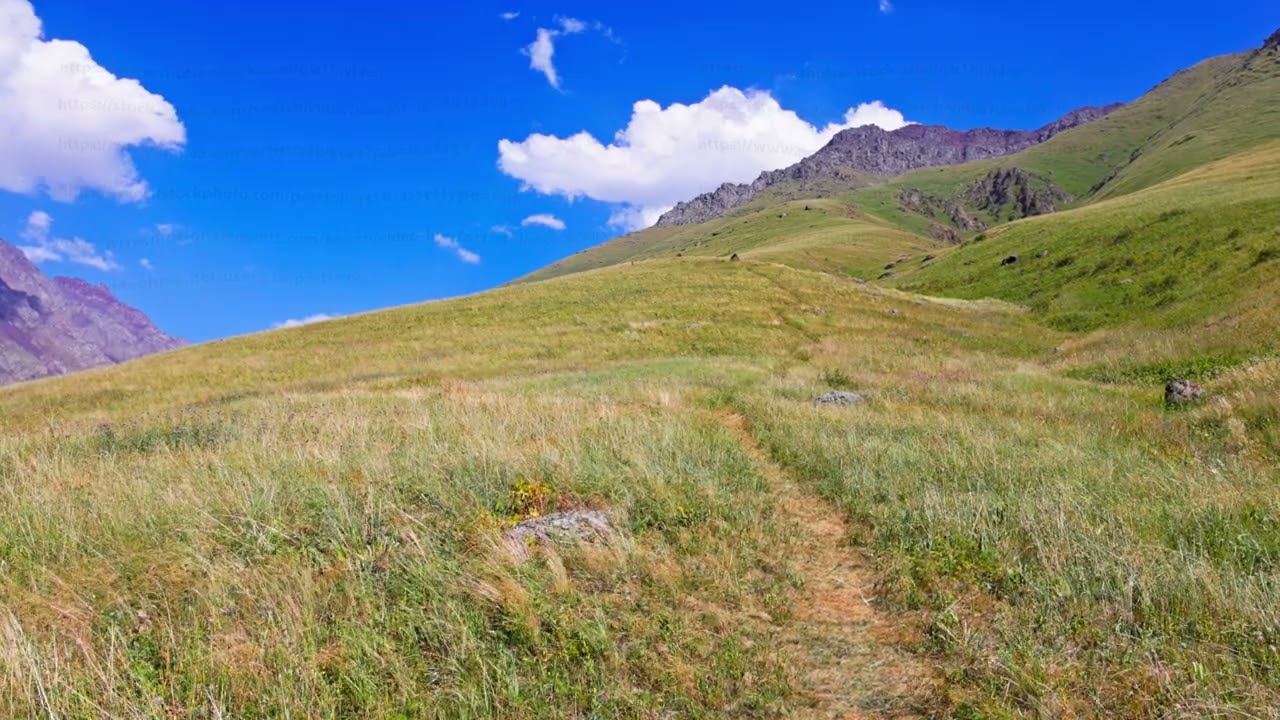 Serene mountain landscape with grassy slopes and dirt path, lockdown shot