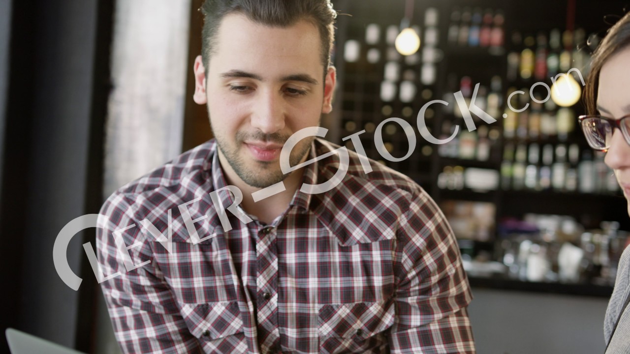Trendy Couple Discussing Project Looking At A Laptop Smiling And Drinking In A Coffee Bar