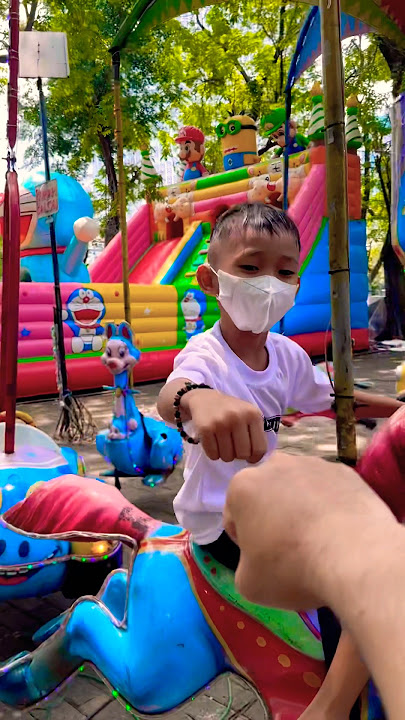 Naik odong odong kuda sambil tos sama kakak seru. Ada istana balon juga di belakang