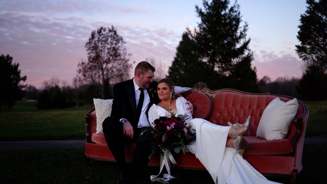 Bride and Groom sitting on a pink sofa, enjoying their company in front of a sunset on the golf course greens at Ravenwood Golf Club in Victor, NY