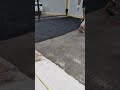 He is applying asphalt coating or liquid tar onto the road surface carefully using a spray tool