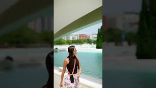 A Stylish Young Woman Enjoying a Leisurely Walk Near Contemporary Architecture in a Vibrant City