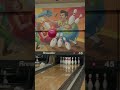 A person in a vintage yellow bowling outfit picks up a pink ball in a brightly lit alley.