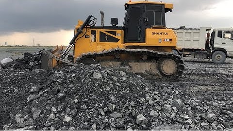 The SHANTUI DH17c2 Bulldozer Machine Pushing Rock For Backfill Uploading Dump Truck On Construction.