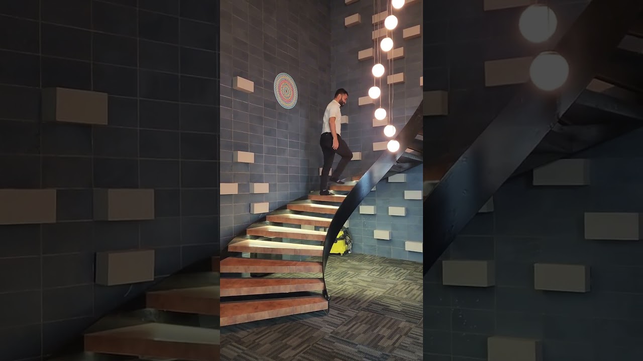 Floating curve of the staircase, the textured dark wall, and the long, hanging pendant lights.