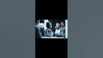 A humanoid robot stands in front of a mirror at a tech expo booth. The handler activates her “self-p