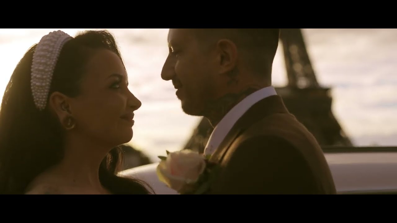 Bride and groom face each other at sunset near the Eiffel Tower, with a boutonniere and pearl headband visible