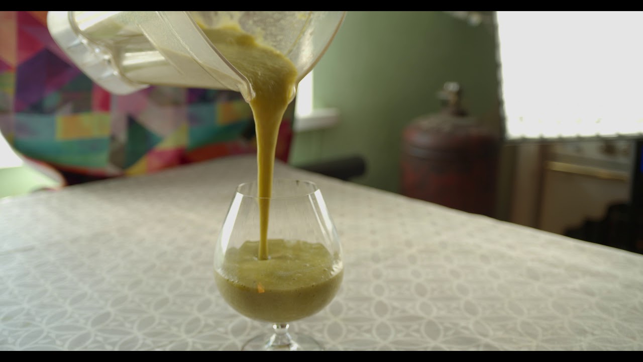 The hostess pours a green smoothie from a blender into a glass.