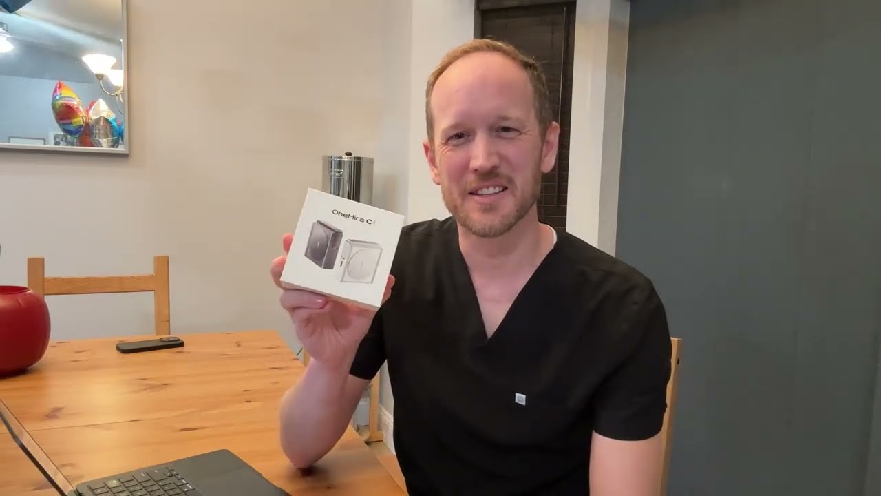 A man in a black shirt holding a black OneMira C1 at a dining table.