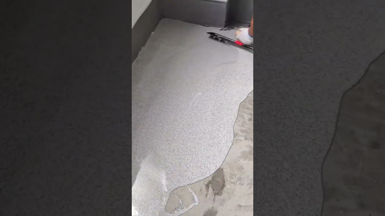 A worker spreading white epoxy flake coating with a squeegee