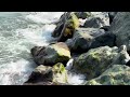Close-up of ocean waves crashing on mossy rocks on a vibrant shoreline.
