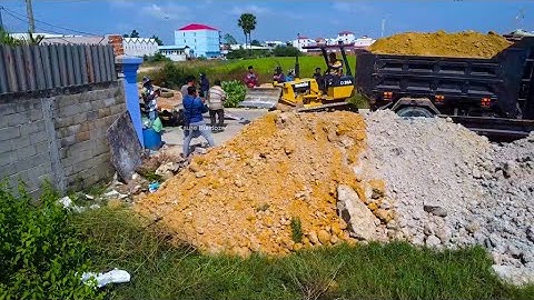 Busy landfill by many dump truck unload soil to delete flooded with old small power dozer KOMATSU