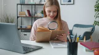 Curious kid watching pictures in book using magnifying glass sitting at table in apartment