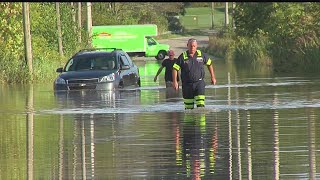 Tow truck driver helps elderly man out of car on flooded Warren road