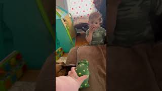 Mom put green pig toy on couch and squeezes it then boy watching TV gets scared and starts to cry