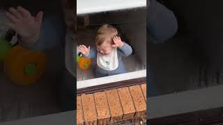 Baby leans on window inside house and guy sprays garden hose at window from outside